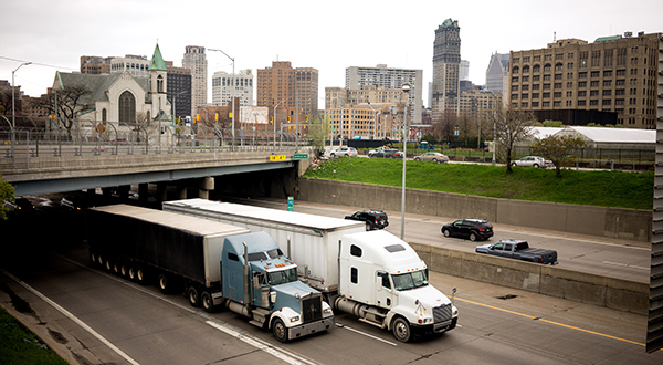 Semi-trucks on a highway with a city in the background.
